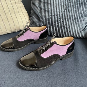 May include: A pair of black and purple lace-up shoes with a patent leather toe cap. The shoes are on a blue couch.