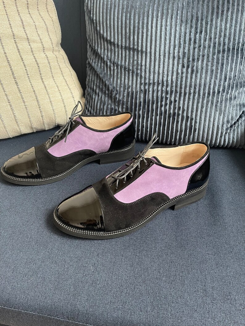 May include: A pair of black and purple lace-up shoes with a patent leather toe cap. The shoes are on a blue couch.