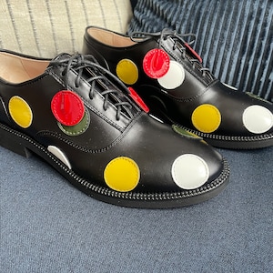 May include: Black leather lace-up shoes with white, yellow, and red polka dots.