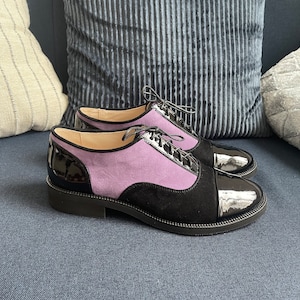 May include: A pair of black leather lace-up shoes with a purple suede panel and a patent leather toe cap.