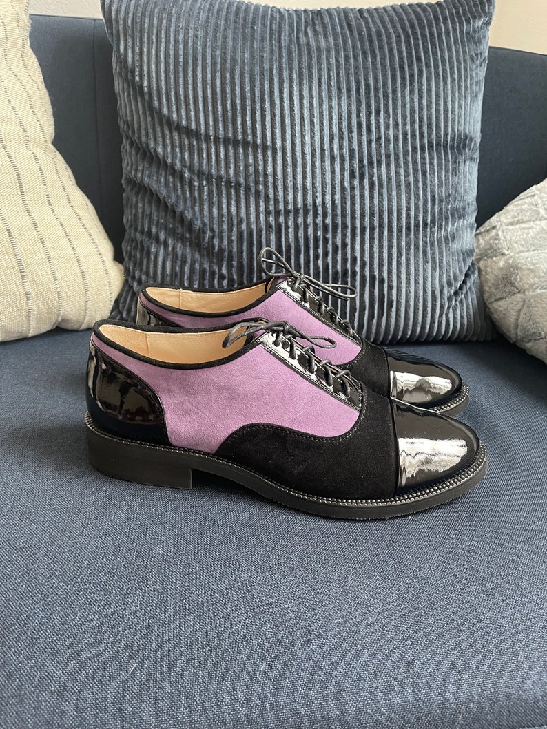 May include: A pair of black leather lace-up shoes with a purple suede panel and a patent leather toe cap.
