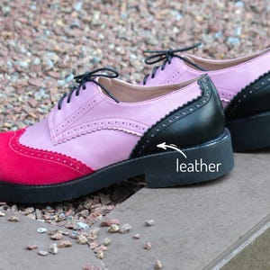 Pu&ograve; includere: Un paio di scarpe Oxford in pelle rosa, nera e rossa con chiusura a lacci. Le scarpe hanno una suola in gomma nera e una fodera in pelle bianca. La parola "pelle" &egrave; scritta sulla suola della scarpa.