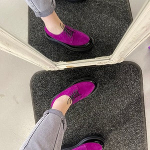 May include: A pair of purple suede shoes with black patent leather toes and black laces. The shoes have thick black soles.