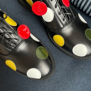 May include: A pair of black leather shoes with white, yellow, green, and red polka dots. The shoes have laces and are tied.