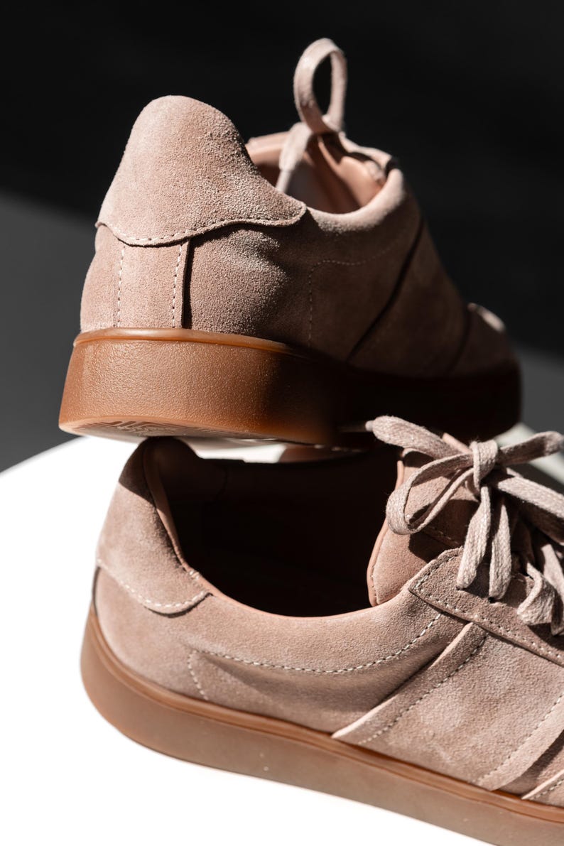 May include: A pair of light brown suede sneakers with a gum sole. The sneakers have a lace-up closure and a classic design.
