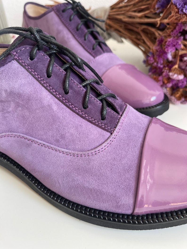May include: Purple suede and patent leather lace-up shoes with a rounded toe.