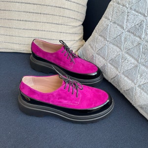 May include: A pair of fuchsia suede lace-up shoes with black patent leather trim and a chunky black platform sole.