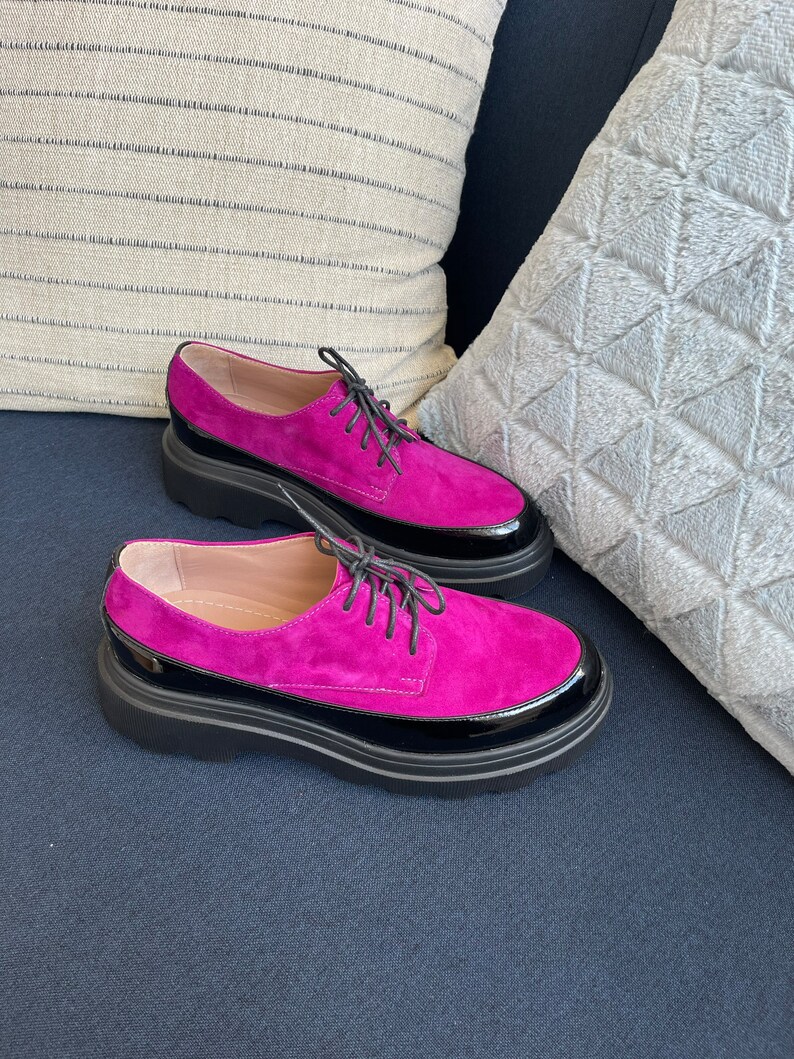 May include: A pair of fuchsia suede lace-up shoes with black patent leather trim and a chunky black platform sole.