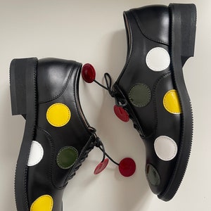 May include: A pair of black leather lace-up shoes with white, yellow, and green polka dots. The shoes have a rounded toe and a thick sole.