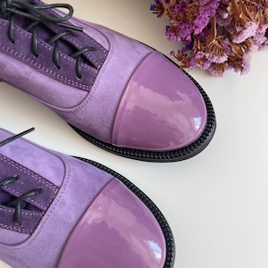 May include: A pair of purple suede and patent leather lace-up shoes with black laces. The shoes have a rounded toe and a black rubber sole.