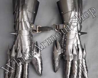 Könnte beinhalten: Paar beweglicher Stahl-Fausthandschuhe mit stacheligen Knöcheln und Handgelenksriemen. Die Fausthandschuhe sind dunkelgrau und scheinen aus überlappenden Metallplatten zu bestehen. Der Text "White Armour Shop" ist sichtbar.