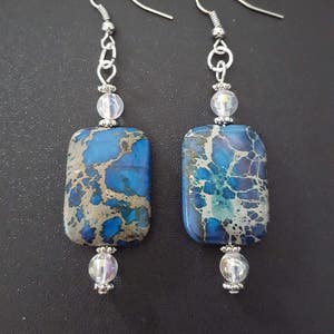 May include: A pair of silver dangle earrings with blue and white jasper stone rectangular pendants and clear crystal beads.