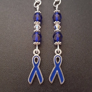 May include: A pair of silver earrings with blue ribbon charms. The earrings are made with blue and clear crystal beads.