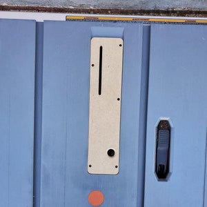 May include: A close-up of a blue table saw with a wooden insert and a black lever. The table saw has a red circle on the surface.