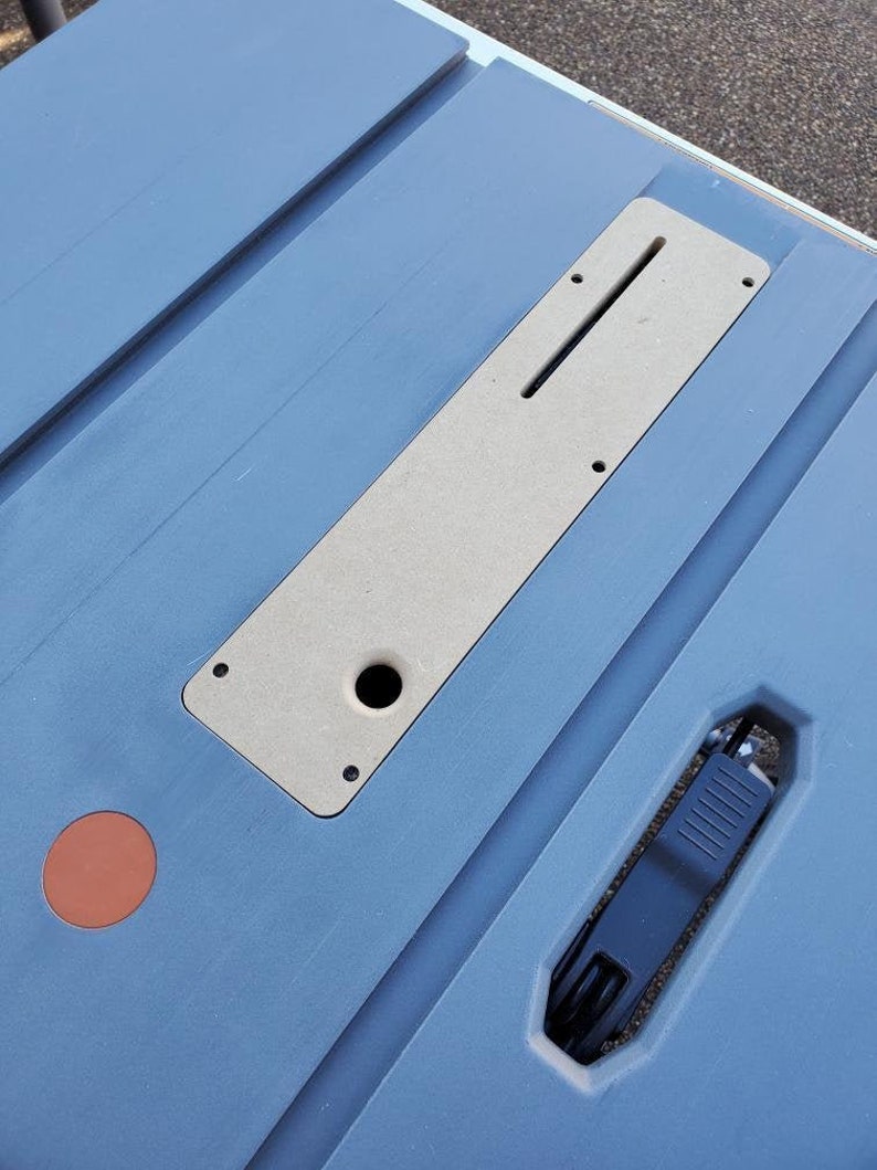 May include: A blue table saw with a beige insert for a router or other tool. The insert has a slot and a hole for a tool. The table saw has a black handle.