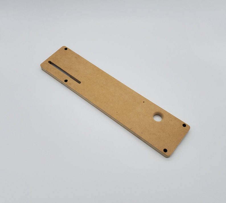 May include: A light brown wooden template with a slot and a hole. The template is designed for woodworking projects.