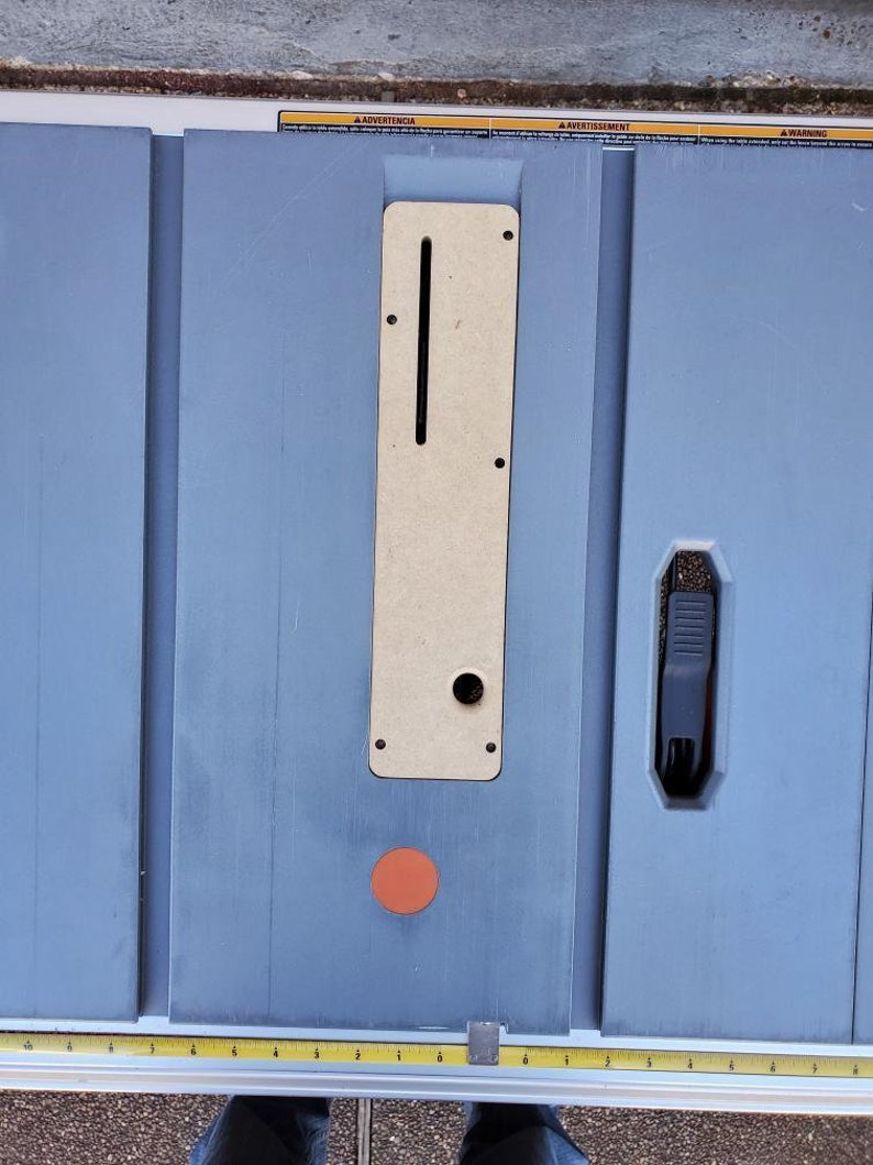 May include: A close-up of a blue table saw with a wooden insert and a black lever. The table saw has a red circle on the surface.