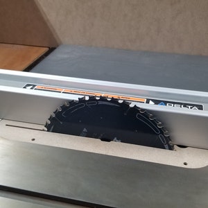May include: A silver table saw with a black saw blade and a silver fence with the word "DELTA" printed on it.