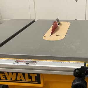 Puede incluir: Una sierra de mesa DeWalt amarilla y negra con una mesa de trabajo gris y una hoja de sierra roja. La hoja de sierra es parcialmente visible a trav&eacute;s de una abertura circular en la mesa de trabajo.