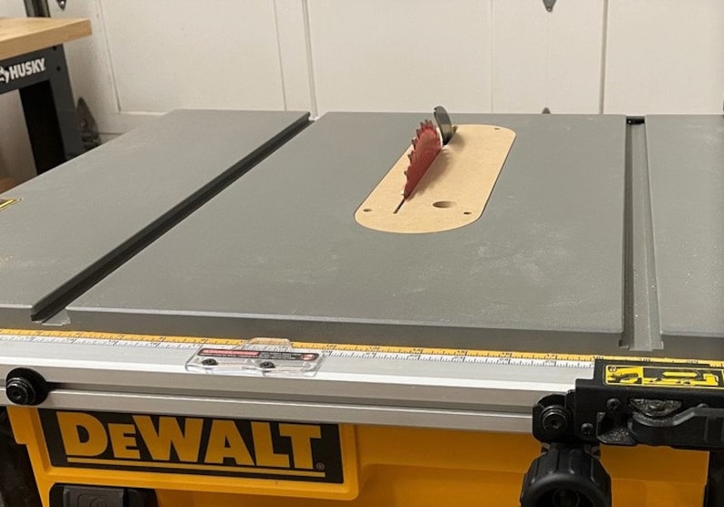 Puede incluir: Una sierra de mesa DeWalt amarilla y negra con una mesa de trabajo gris y una hoja de sierra roja. La hoja de sierra es parcialmente visible a trav&eacute;s de una abertura circular en la mesa de trabajo.