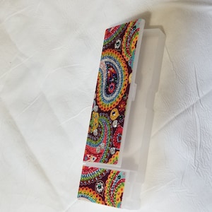 May include: A clear plastic case with a colorful paisley design. The design features red, yellow, blue, and green patterns with sparkling embellishments. The case is open, revealing its interior.