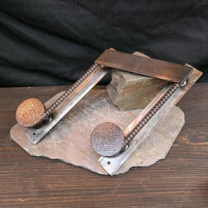 May include: A handcrafted metal sculpture featuring two musical note shapes. Each note has a textured, spherical head and a stem made of twisted metal. The sculpture rests on a natural stone base, with a dark background.