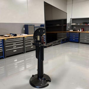 May include: A large, black industrial machine with a tall, vertical design. The machine has a circular component at the top and a wide, circular base. It stands on a gray floor in a workshop setting.