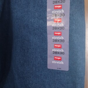 Puede incluir: Un primer plano de una etiqueta de mezclilla azul con el texto "Wrangler" y "stretch 38X30" repetido varias veces. La etiqueta tambi&eacute;n incluye el texto "SUSO".