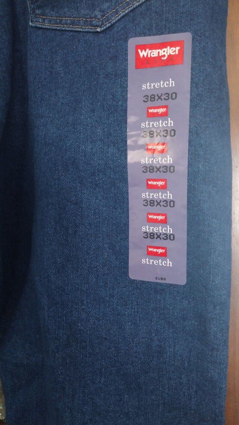 Puede incluir: Un primer plano de una etiqueta de mezclilla azul con el texto "Wrangler" y "stretch 38X30" repetido varias veces. La etiqueta tambi&eacute;n incluye el texto "SUSO".