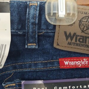 Puede incluir: Un par de pantalones vaqueros azules con una etiqueta blanca que dice "Wrangler" y "85900DW 38 X 30 STRETCH" y una etiqueta marr&oacute;n que dice "Wrangler Authentic Jeans".