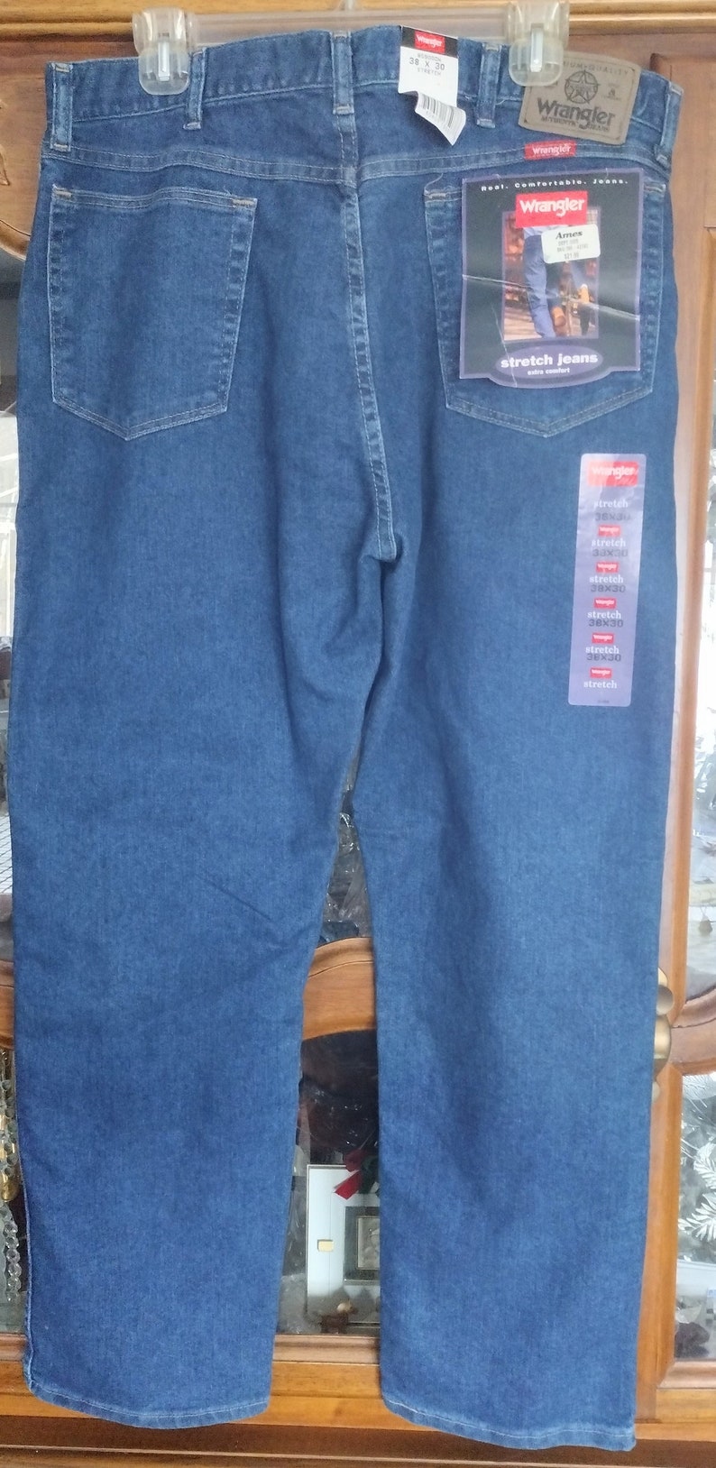 Puede incluir: Un par de pantalones vaqueros azules de mezclilla con una etiqueta de Wrangler. Los pantalones tienen un corte holgado y est&aacute;n hechos con tela el&aacute;stica. La etiqueta dice "Wrangler Stretch Jeans" y "Extra Comfort".