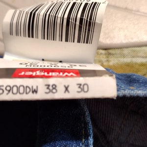 Puede incluir: Primer plano de una etiqueta de mezclilla azul con el texto "Wrangler 85900DW 38 X 30".