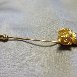 May include: A gold-colored stick pin featuring a detailed ram's head design. The pin has a long, slender shaft and a decorative, rounded end. The ram's head is intricately sculpted, showcasing the horns and facial features. The pin is set against a neutral background.