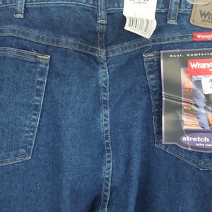 Puede incluir: Un par de pantalones vaqueros azules con un bolsillo trasero y una etiqueta de Wrangler adjunta. La etiqueta dice "Real. Comfortable. Jeans." y "Stretch Jeans Extra Comfort". Los vaqueros son talla 38x30.