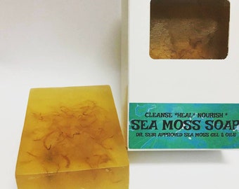 May include: A bar of yellow sea moss soap in a white box with the text "CLEANSE *HEAL* NOURISH * SEA MOSS SOAP DR. SEBI APPROVED SEA MOSS GEL & OILS" printed on the front.