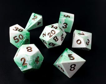 May include: A set of seven green and white dice with gold numbers. The dice are made of a marbled resin and have a variety of shapes, including a d4, d6, d8, d10, d12, and d20.
