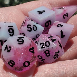 May include: A set of seven pink and blue dice with white and black glitter. The dice are numbered 1-6, 9, 12, 14, 16, 20, and 50.