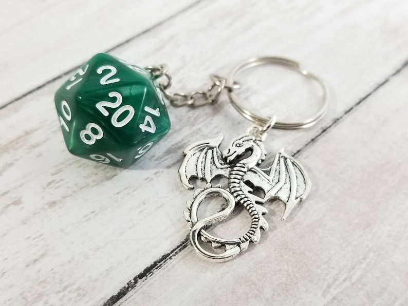 May include: A green 20-sided die with white numbers attached to a silver dragon keychain. The keychain is attached to a silver key ring.