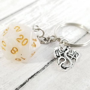 May include: White 20-sided dice keychain with gold numbers and a silver dragon charm.