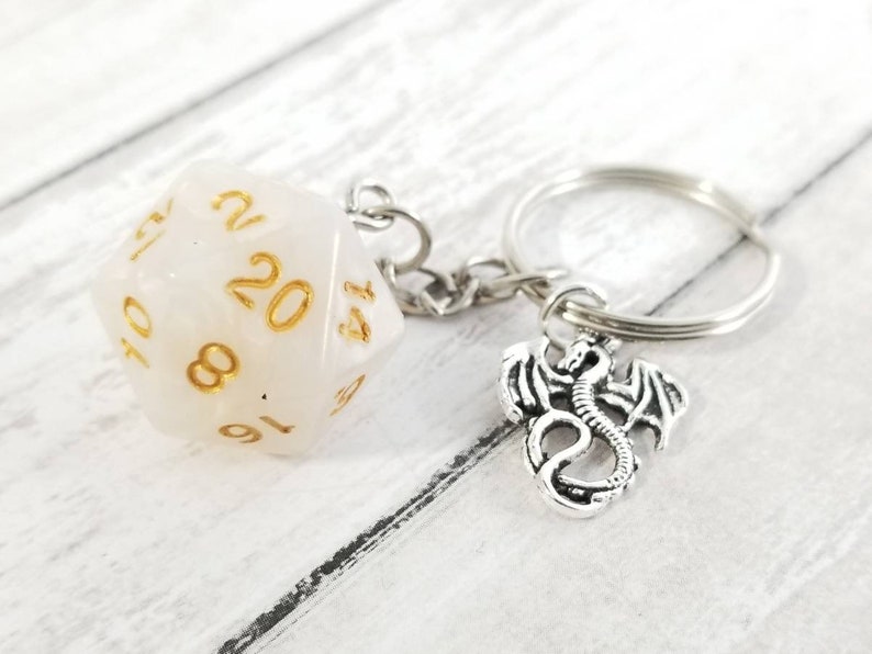 May include: White 20-sided dice keychain with gold numbers and a silver dragon charm.