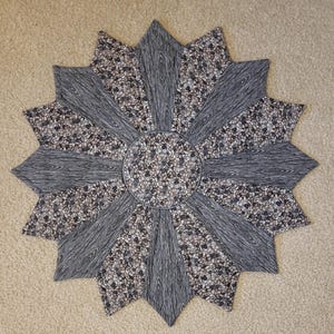 May include: A gray and white star-shaped table runner with a woodgrain pattern. The center of the runner is a circle with a smaller, repeating pattern.