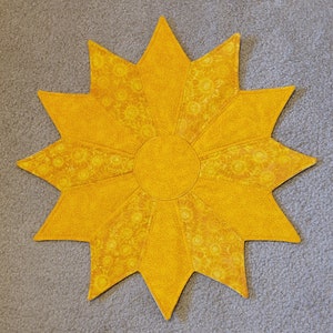 May include: A yellow star-shaped table runner with a sunflower pattern. The center of the runner is a solid yellow circle.
