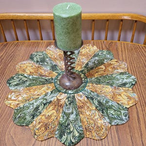 May include: A green and gold marbled fabric table runner with a scalloped edge. A green candle sits on a metal candle holder in the center of the runner.
