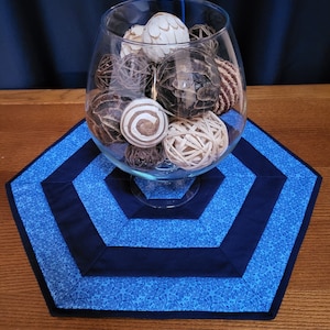 May include: A blue and white hexagonal table runner with a glass bowl filled with decorative balls. The bowl is in the center of the runner.