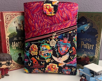 May include: A patterned book sleeve with a black zip and flap closure. The sleeve displays Harry Potter themed imagery. Two Harry Potter books and figurines are in the background.