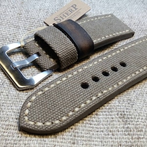 Peut inclure: Un bracelet de montre en toile beige avec des coutures blanches et une boucle en acier inoxydable. Le bracelet est doublé de cuir brun et porte une étiquette de marque "SHERP".