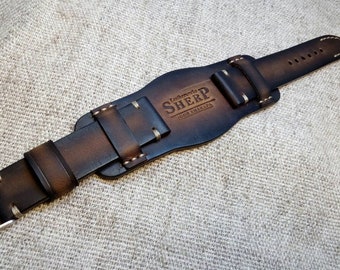 May include: A dark brown leather watch strap with a wide cuff design, featuring a silver-tone metal buckle and light-coloured stitching. The leather is embossed with the text Leatherworks SHERP IGOR SHARAPA in the centre of the cuff section.