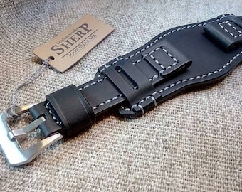 May include: Black leather watch strap with white stitching and a silver buckle. The strap is designed for a large watch face and has a loop for securing the strap.