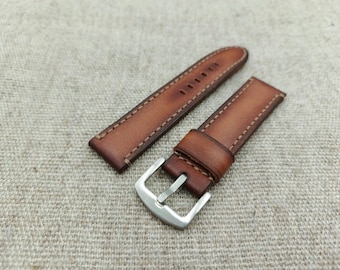 May include: A brown leather watch strap with a silver buckle. The strap is made of a rich, textured leather and features contrasting stitching. The strap is approximately 9 inches long.