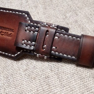 May include: Brown leather watch strap with white stitching and a silver buckle. The strap has the text "MADHOMOL Hand Made" embossed on it.